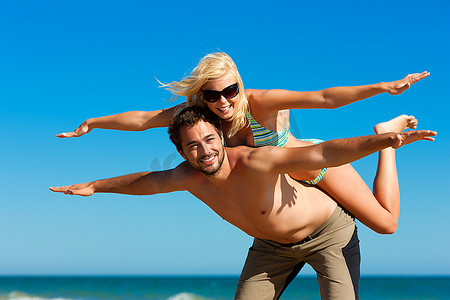 一对相爱的夫妇--一个男人背着他的妻子在海滩度假，他们感到明显的自由和快乐。