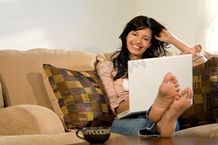 一个美丽的西班牙裔女孩在家里放松，喝着卡布奇诺，使用着她的笔记本电脑。
