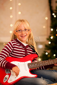 一个小女孩拿着她的吉他--大概是礼物--在圣诞树前