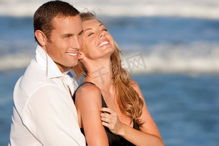 一对年轻的男女在海滩上拥抱着，笑着，就像一对幸福的浪漫情侣