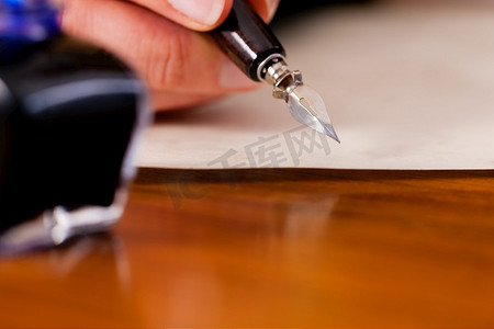 一个女人(只有一只手被看到)用钢笔和墨水在纸上写字，前景中她有一个墨水罐
