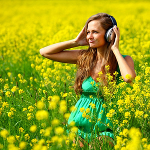花园音乐摄影照片_年轻女子与耳机听音乐的油籽开花领域