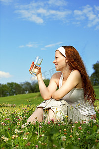 美丽的女人坐在草坪上喝水