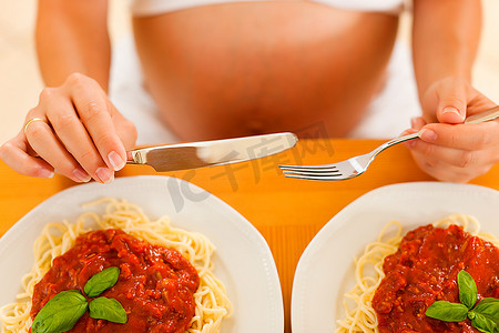 两个饥饿的孕妇吃两份意大利肉酱面在她面前