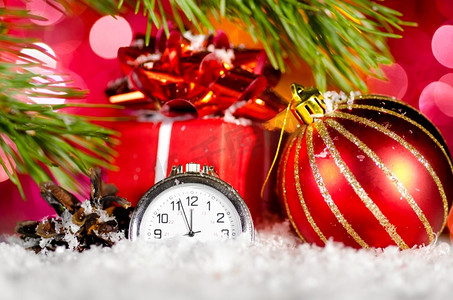 礼品盒、球和时钟在雪地上，背景模糊的圣诞树树枝
