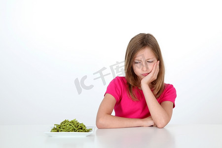 厌恶摄影照片_年轻女孩厌恶地看着一盘青豆