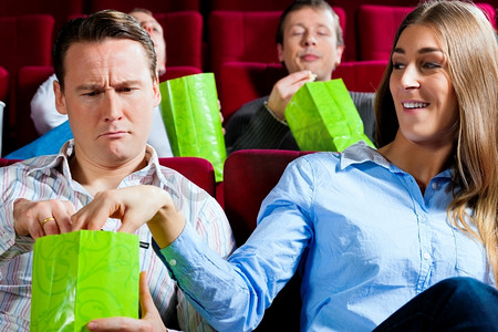 一对情侣在电影院看电影；他们吃爆米花