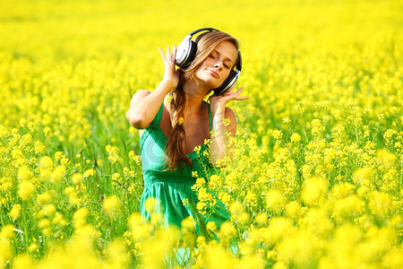 戴着耳机的年轻女子在油籽花田里听音乐