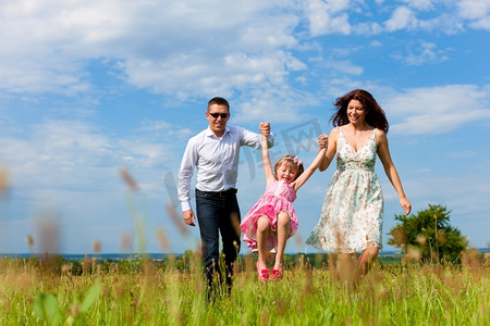 草地玩的孩子摄影照片_快乐的家庭-母亲，父亲，孩子-在夏天跑过一片绿色的草地