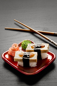 一双筷子和一个方形盘子的特写镜头，里面有两块黑玉米粉，芥末和生姜。