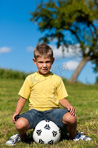 小男孩拿摄影照片_快乐的小男孩拿着足球坐在草地上玩耍