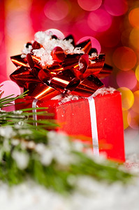 雪地上的红色礼品盒，背景模糊，圣诞树树枝