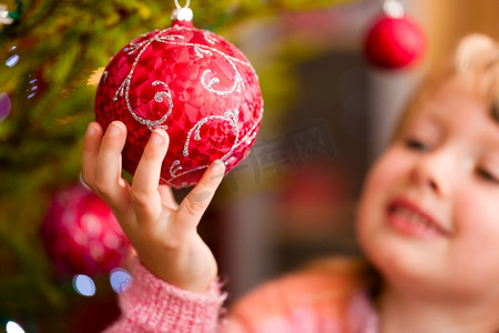小玩意儿摄影照片_年轻女孩手持圣诞小玩意儿，帮忙装点圣诞树。