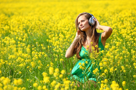 戴着耳机的年轻女子在油籽花田里听音乐