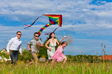 一家人放风筝摄影照片_幸福的一家人--母亲、父亲、孩子--夏天在一片绿色的草地上奔跑；他们在放风筝