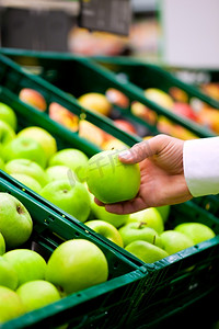 水果超市摄影照片_只有男人的手--在一家超市货架上，他正在查看苹果。