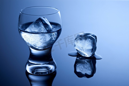 杯子加冰块摄影照片_一个优雅的小酒杯，加伏特加和冰，在反光表面上还有一个融化的冰块。