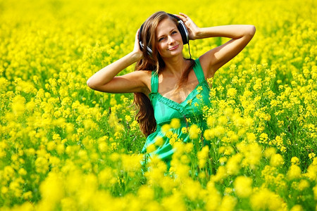 年轻女子与耳机听音乐的油籽开花领域