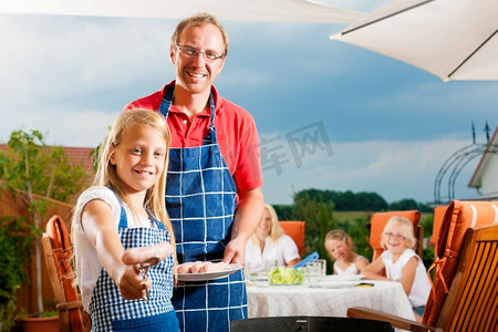 烧烤聚会摄影照片_快乐的一家人在夏天烧烤；父亲和孩子站在烧烤架上