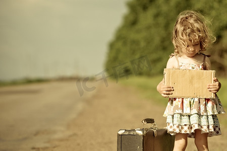 孤零零的女孩提着行李箱站在路上，手里拿着纸，手里拿着版面