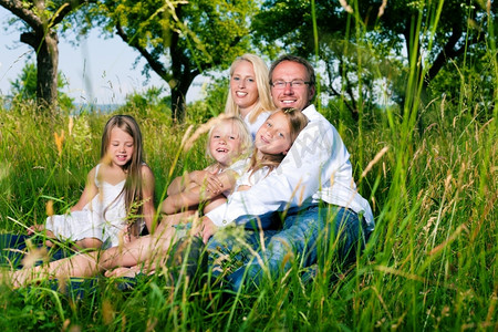 女儿们摄影照片_夏天和女儿们坐在草地上的幸福家庭