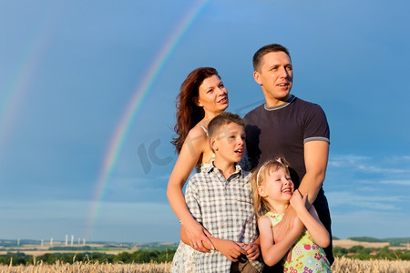 幸福的家庭-母亲，父亲，孩子们-站在彩虹下在夏天展望辉煌的未来
