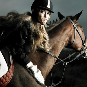 优雅的女人穿着黑色大衣骑在棕色的马上