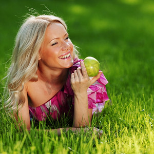 躺在绿草地上的金发女郎手里拿着一个苹果