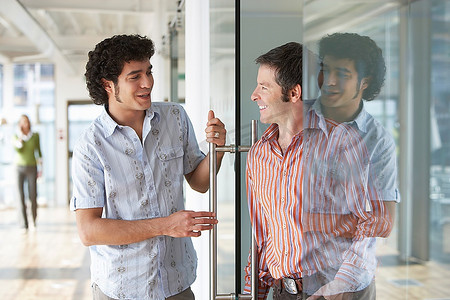 竖纹长虹玻璃摄影照片_两名上班族在办公室的玻璃门前交谈