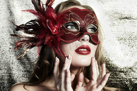 神秘面具人摄影照片_金色背景下戴着神秘的红色威尼斯面具的年轻漂亮女子