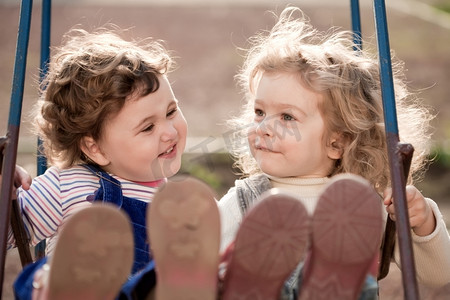 双胞胎婴儿姐妹玩秋千在秋季公园