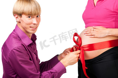 快乐的男人在解开孕妇的肚子上的红丝蝴蝶结