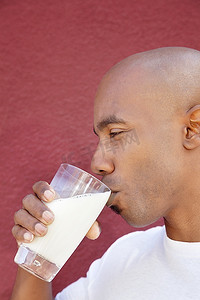 光头喝酒摄影照片_一名非洲裔美国男子在彩色背景下喝牛奶的侧视