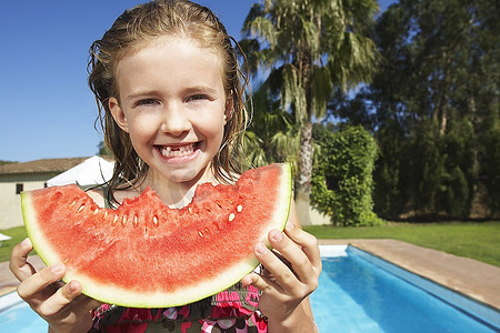 女孩(5-6)在游泳池边吃西瓜的写真
