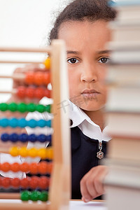 一个年轻漂亮的混血非裔美国女孩在学校教室里用算盘看书，面前放着一堆书
