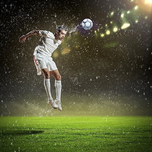 在雨中的体育场用头击球的白色衬衫的足球运动员