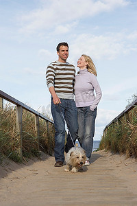一对夫妇在海滩木板路上遛狗