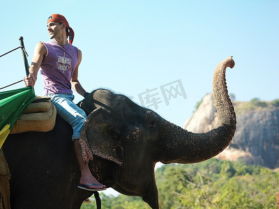 骑着大象侧视的年轻人在背景中俯瞰肩上的群山