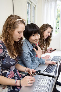 三位女性朋友使用笔记本电脑和手机