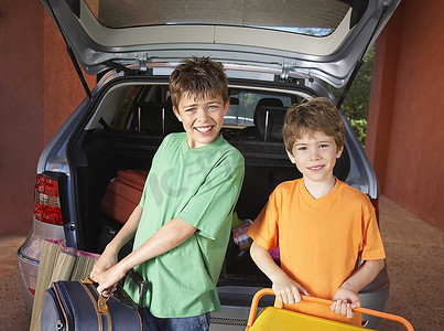 肖像两个男孩（6-11）携带行李箱在汽车前面