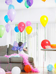 年轻女孩（7-9）坐在沙发与气球佩带仙女翅膀背面视图