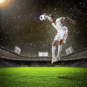 人在雨中摄影照片_在雨中的体育场用头击球的白色衬衫的足球运动员