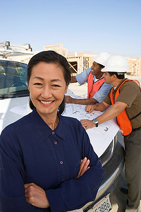 两名建筑工人在建筑工地看图纸和建筑师通电话