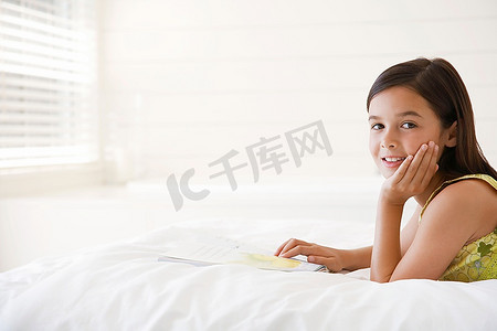 女孩仰卧在床上读故事书，头和肩膀