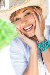 在热带海滩的棕榈树下拍摄的一位戴着草帽的混血美女笑着玩得很开心