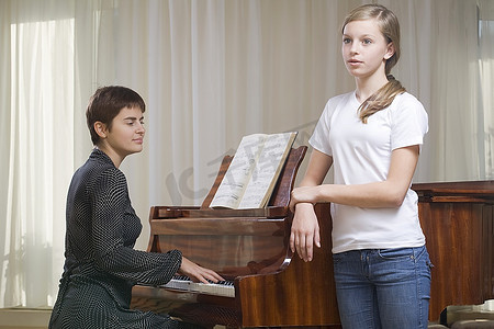 女孩(13-15岁)在钢琴老师的伴奏下唱歌