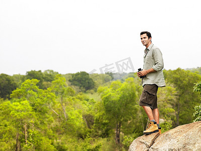 一名中年男子手持双筒望远镜站在岩石上看风景