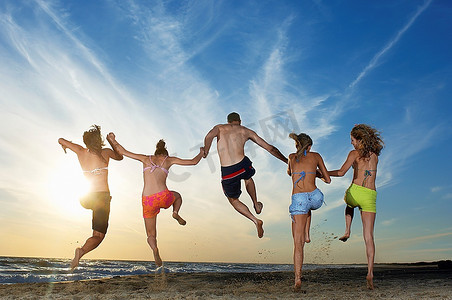 男人和四个女人在海滩上奔跑和跳跃，后景