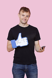 一位快乐的年轻人的肖像，粉色背景上拿着手机的假Like按钮