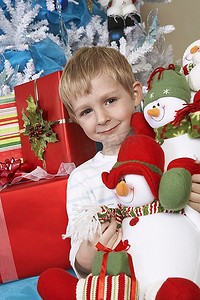 男孩(5-6岁)在圣诞树前抱着填充雪人，肖像